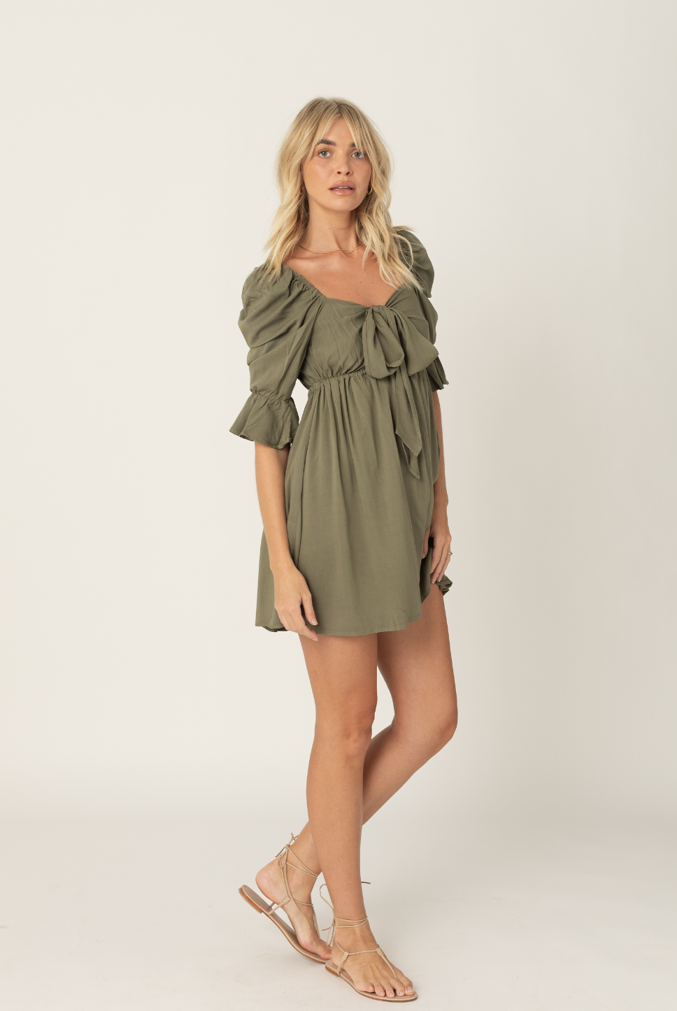 Khaki green mini empire waist dress with a bow tie enclosure in the front. Elastic bust and sleeves for a forgiving fit. Can be worn off the shoulder or backwards. Is breastfeeding and bust friendly.